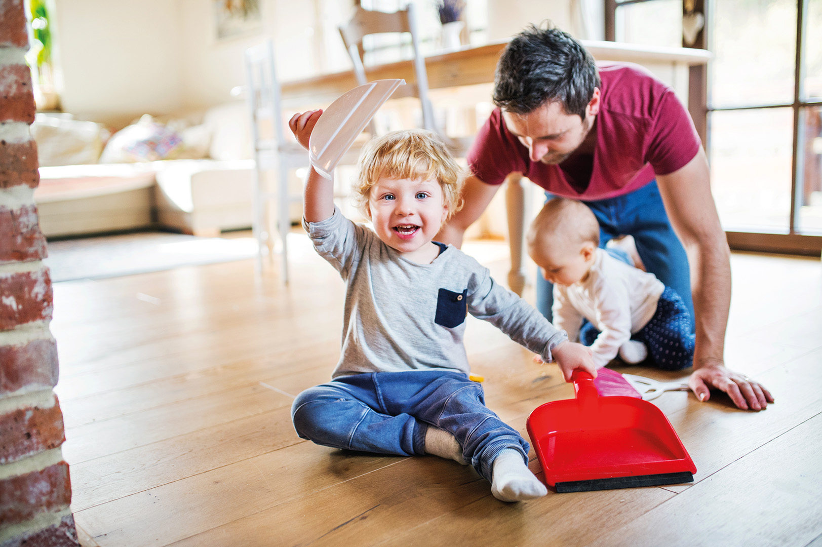 Young boy sitting on floor holding a dustpan. Sweeping is one of the many age-appropriate chores suitable for preschoolers.
