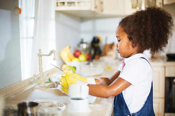 Age-appropriate chores for primary school kids. Young girl standing in front of sink doing the dishes