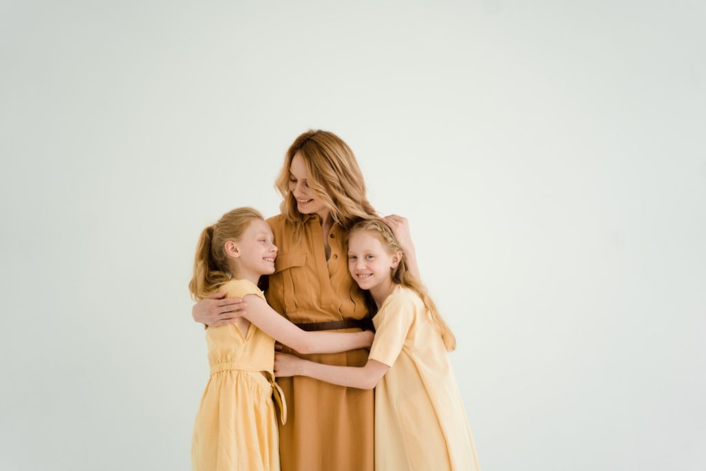 Two young girls hugging mum around the waist
