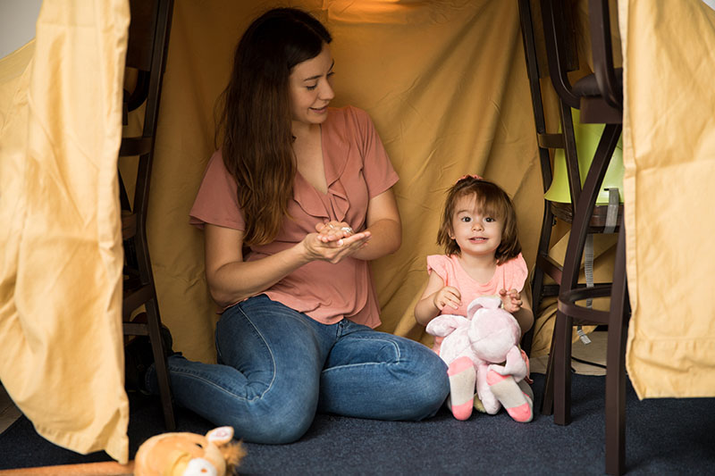 Indoor activities for kids - mum and young daughter hiding in a cubby house made from draping sheets over furniture