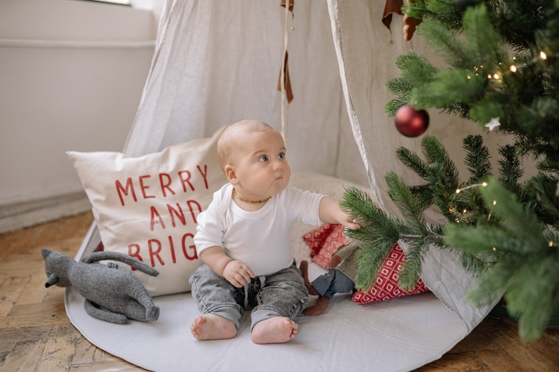 baby sitting in an indoor teepee next to a christmas stree