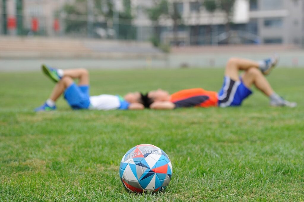 football on grass, with two kids in jersey lying down in the background