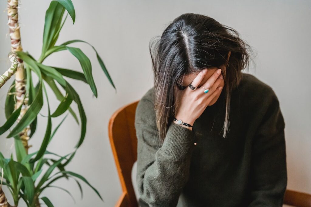 Tired woman sitting on a chair looking down, resting her forehead on her raised hand.